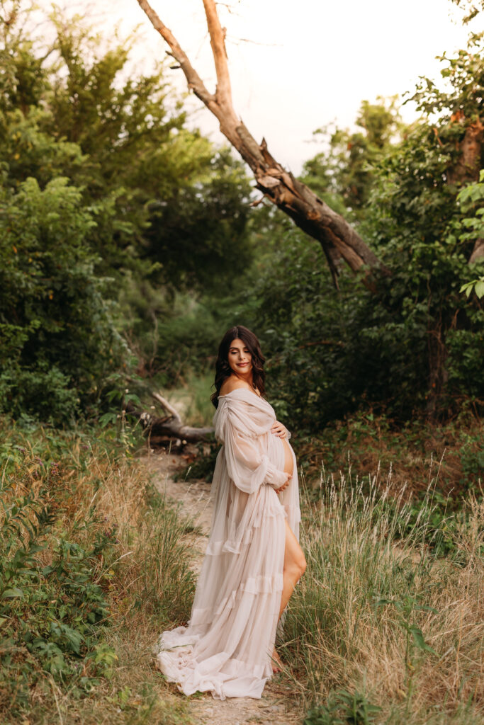 Pregnant mother wearing a romantic flowy gown on the nature trail at Northwest Community Park in Keller, TX. 