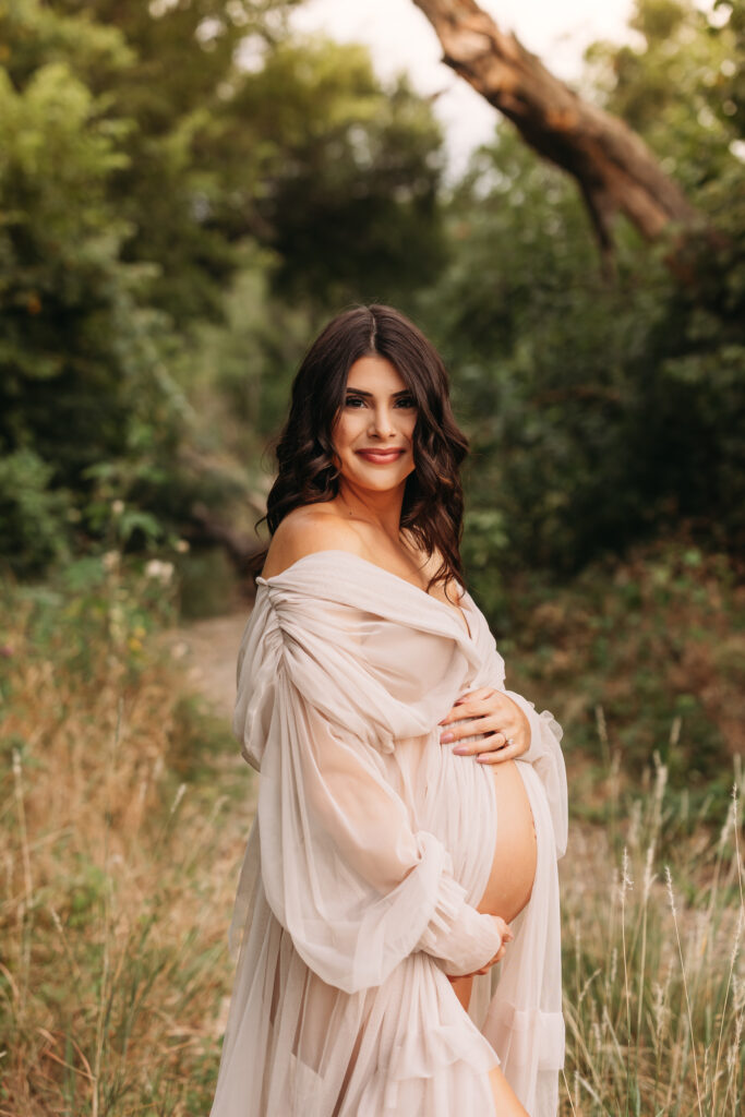 Pregnant mother holding her baby belly wearing a floor length gown at Northwest Community Park. 