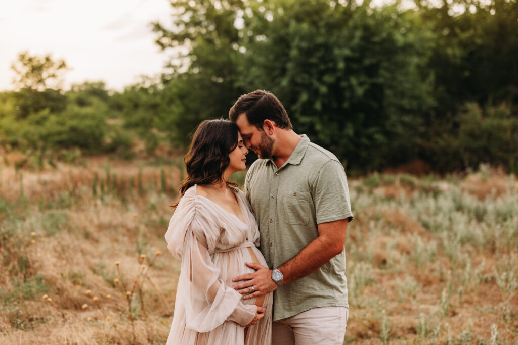 Expecting mother and father leaning head to head with their eyes closed as the husband places a hand on her baby bump. 