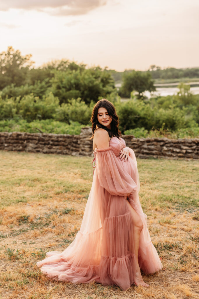 Pregnant mother wearing a pink ruffle gown illuminated by a gorgeous Texas sunset behind her. 