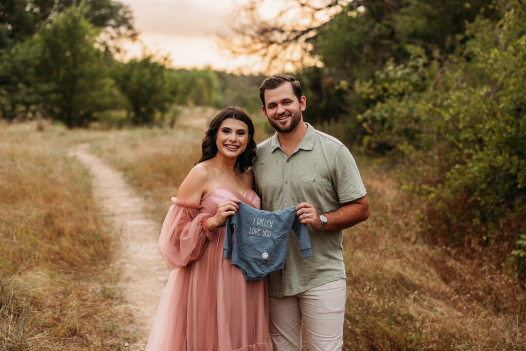 Expecting parents hold up a baby onesie to celebrate their growing family. 