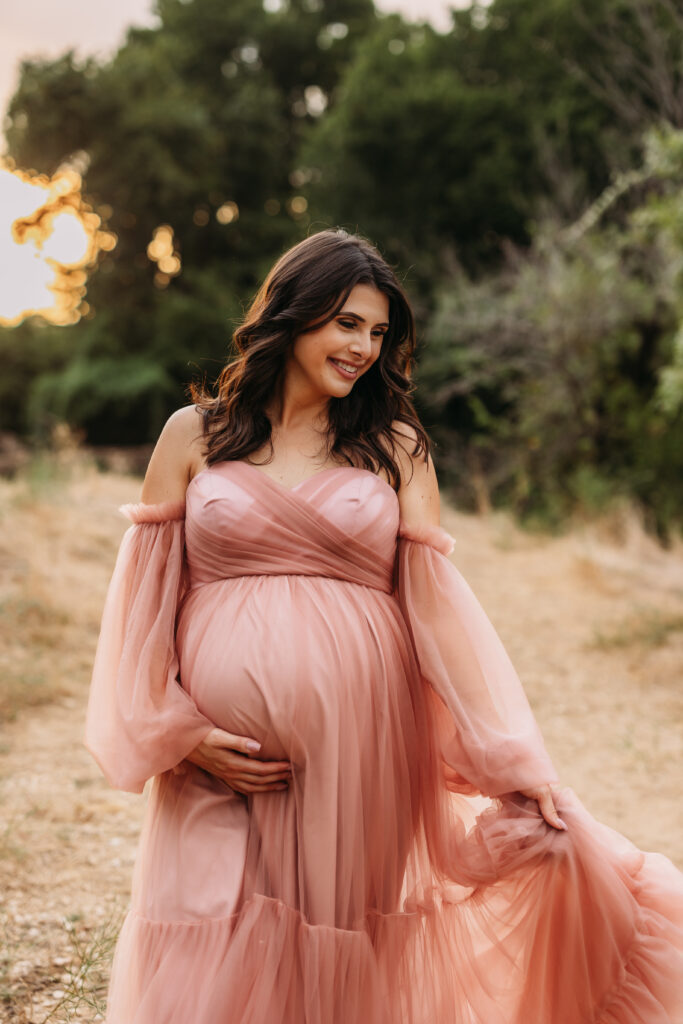 Expecting mother smiling and wearing a lovely blush pink gown. 